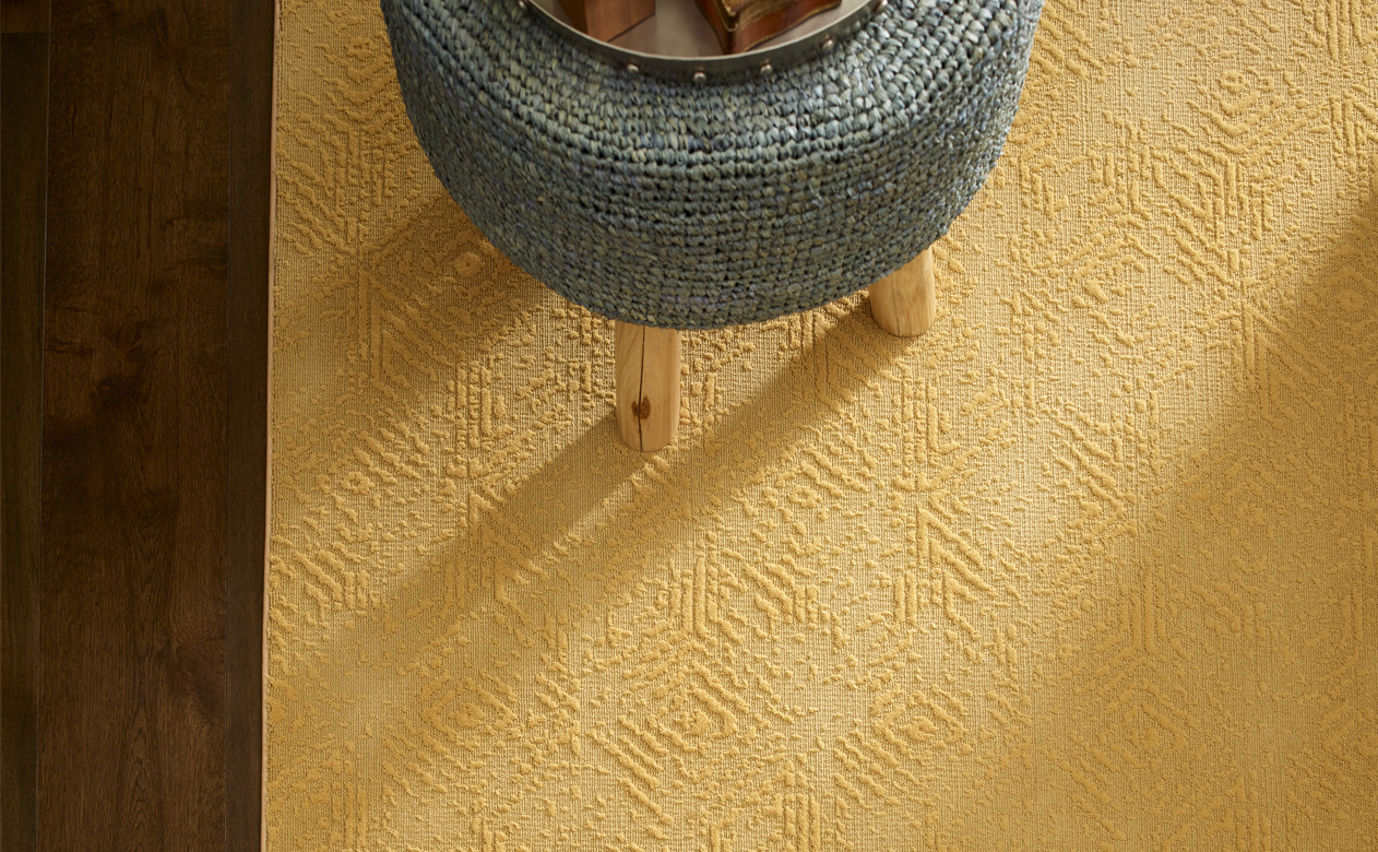 yellow textured area rug in living area with gray stool and dark brown wood flooring